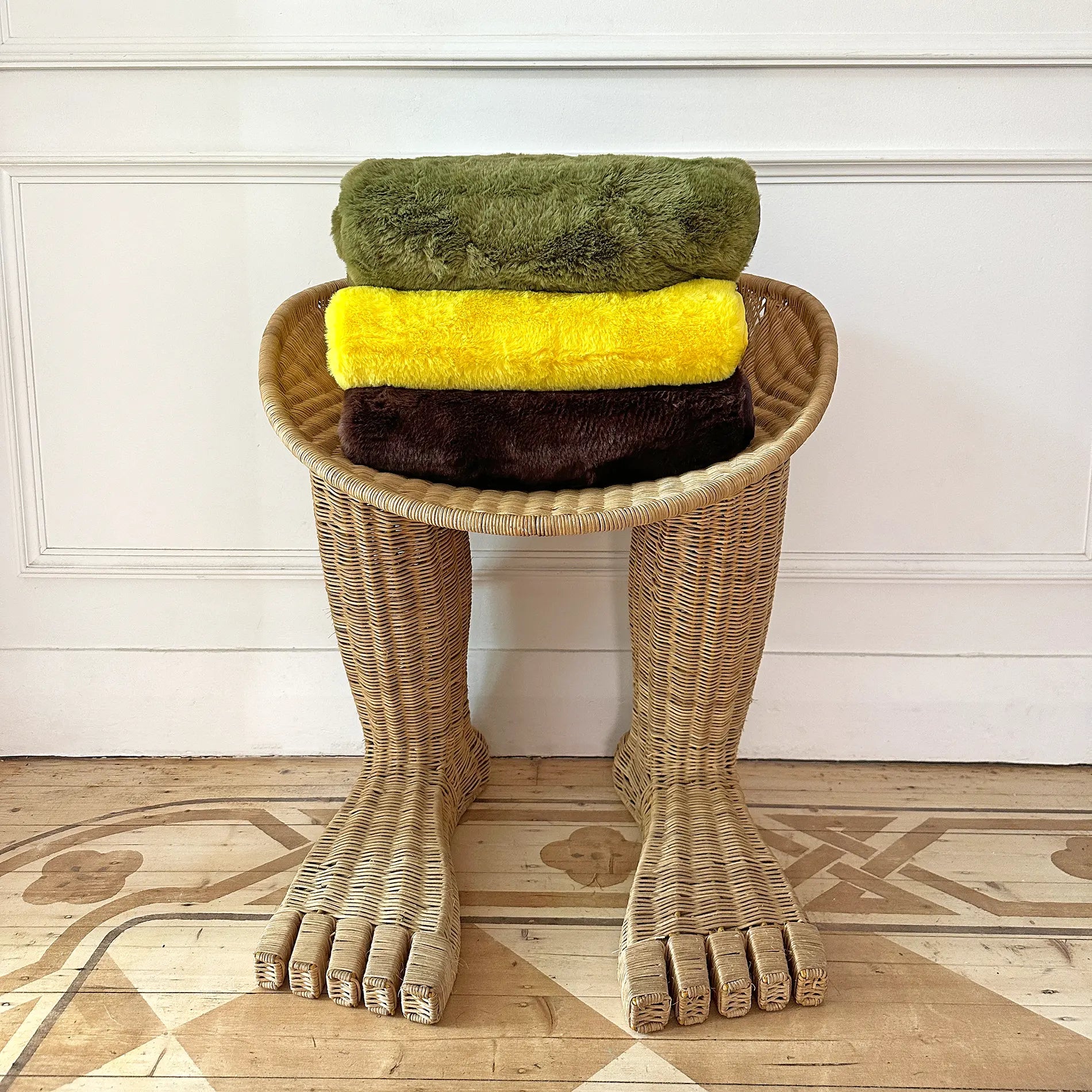 Stack of green, yellow, and brown dog blankets on a unique wicker chair with foot-shaped legs