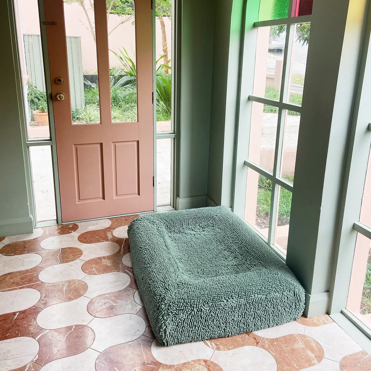 Green dog bed placed on a patterned floor near a door