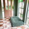 Green dog bed placed on a patterned floor near a door