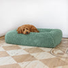 A Labradoodle resting on a green pet bed