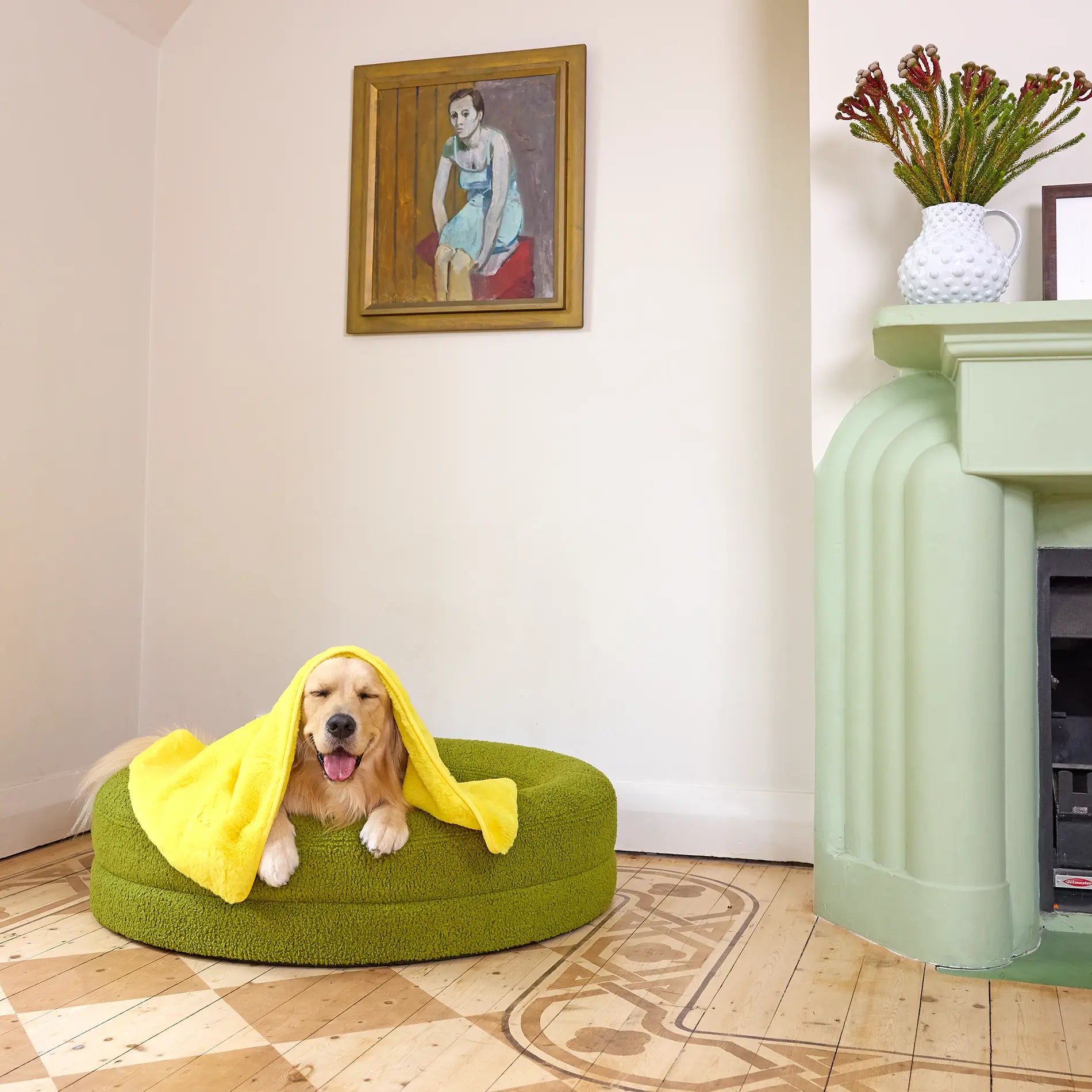 Golden Retriever relaxing on a green pet bed with a yellow towel draped over its head