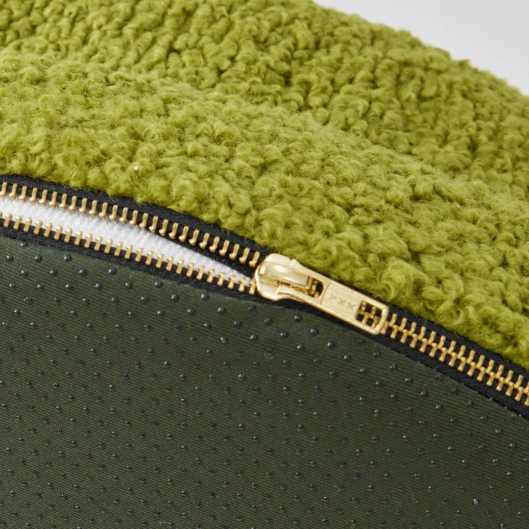 Close-up of a green dog bed with a textured cover and a gold zipper